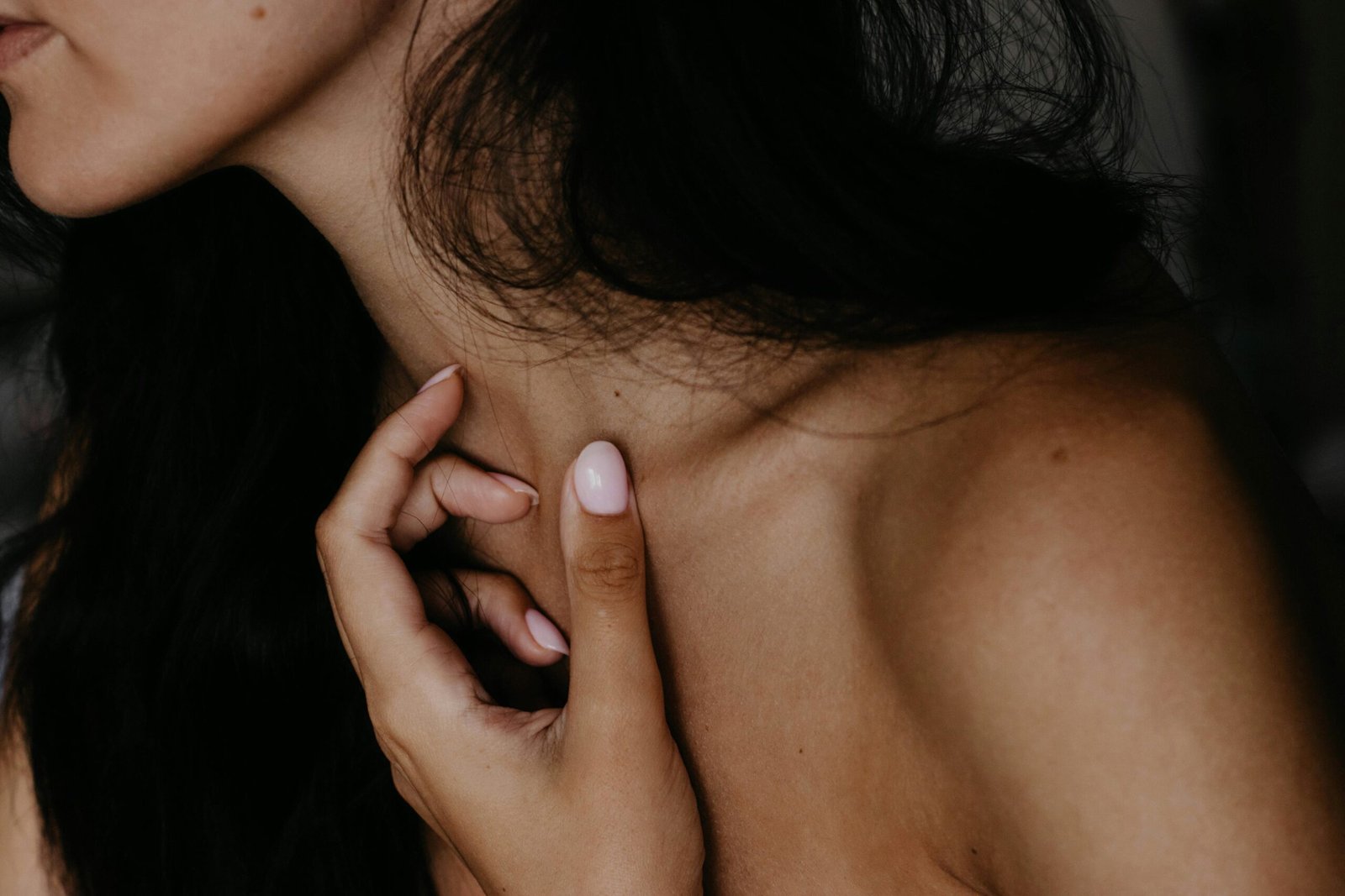 Artistic close-up photo of a woman's neck and hand with a focus on skin texture and nails.